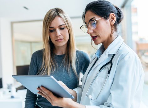 Shot of beautiful female doctor talking while explaining medical treatment with digital tablet to patient in the consultation.