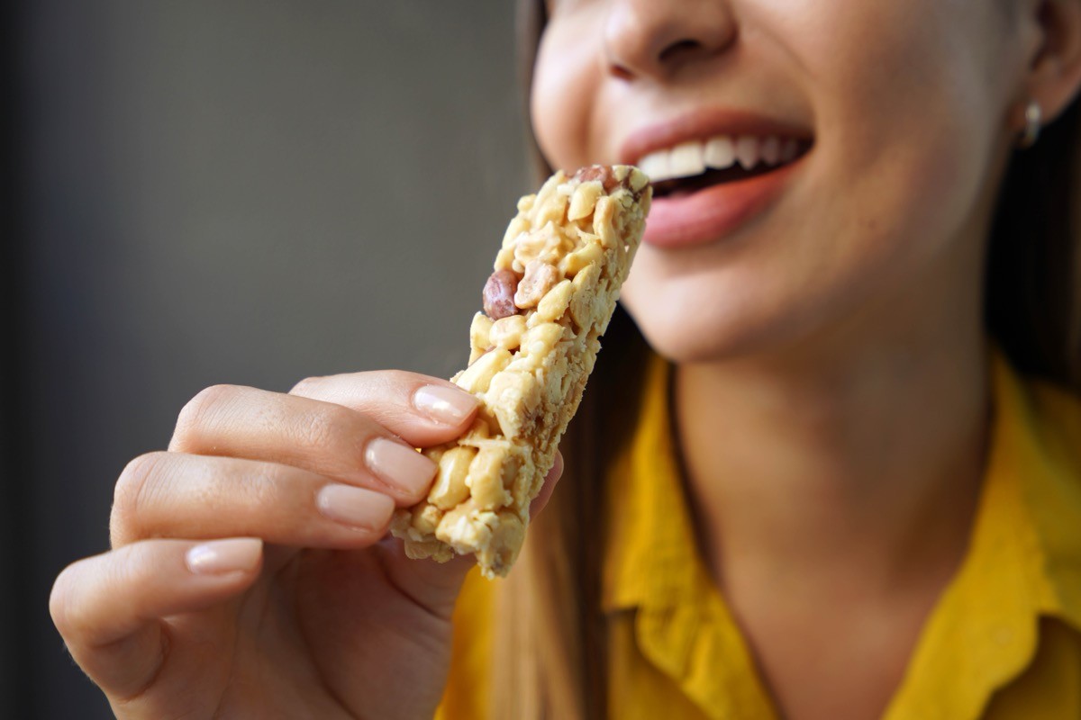Young,Woman,Eating,A,Nuts,Cereal,Bar,Without,Sugar,On