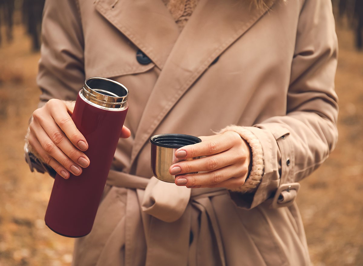 Young woman with thermos drinking hot tea in forest, closeup