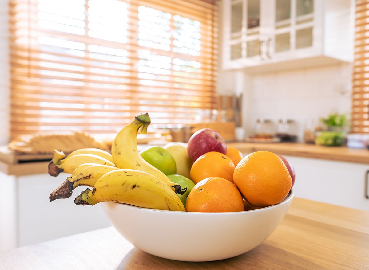 Short of Basket and fresh fruits on wooden table in kitchen at home. Mix variety of fresh juicy colorful healthy fruits in basket on dining counter in house.