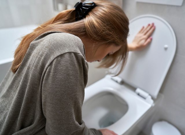 Woman bending over toilet and having a nausea, vomit, vomitting, sick, bathroom