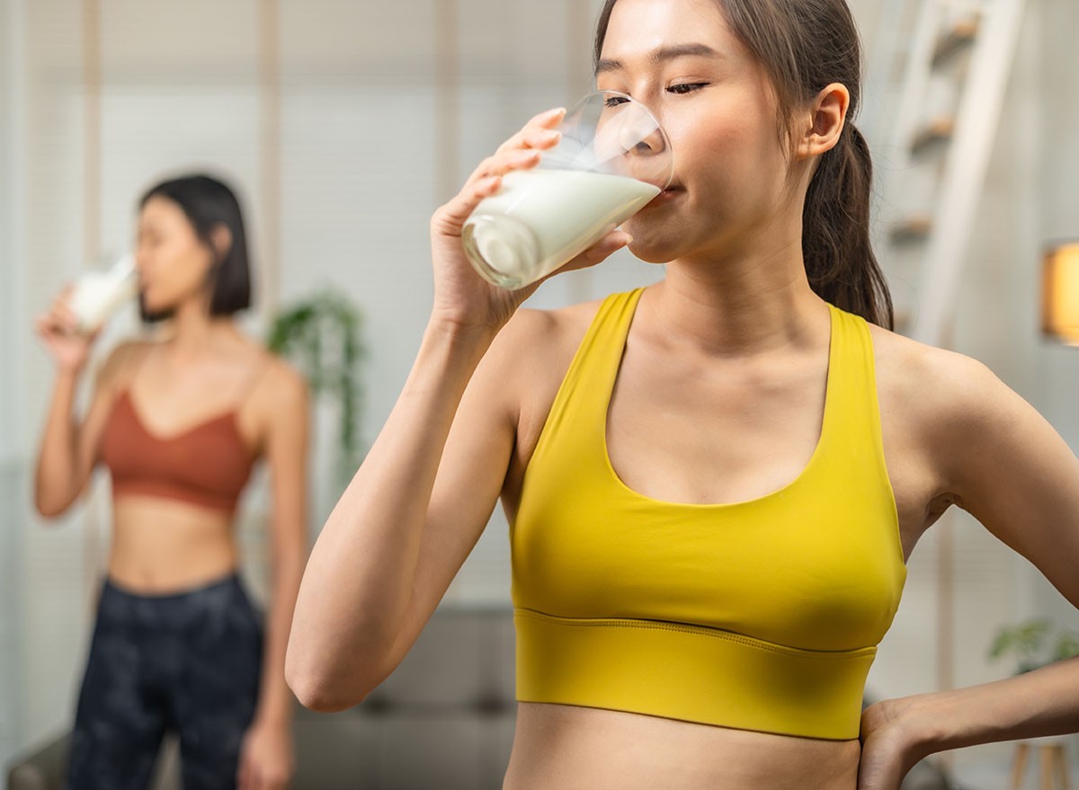Attractive fitness asian woman finishing workout and drinking protein milk shake vitamins after training at home. Bodybuilding. Healthy lifestyle.