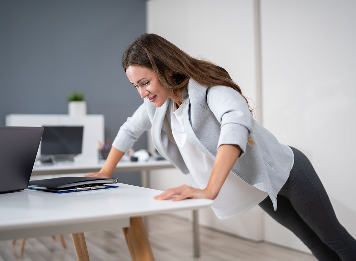 Side View Of A Young Businesswoman Doing Push Up On Office Desk