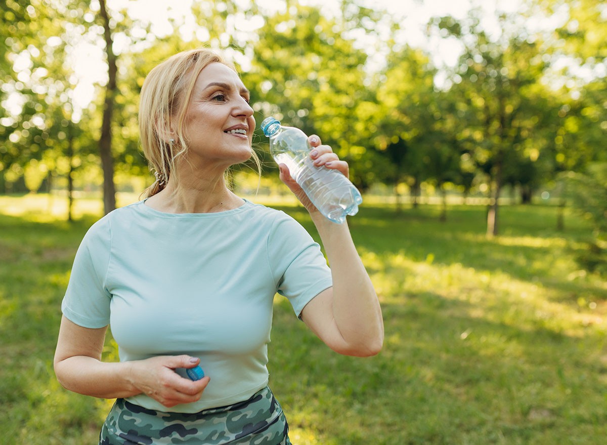 Mature woman drinks water while exercising in the park. The concept of a healthy lifestyle. Copy space