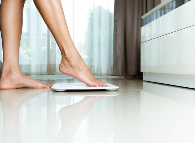 Female leg is stepping on white bathroom scales at home, weight