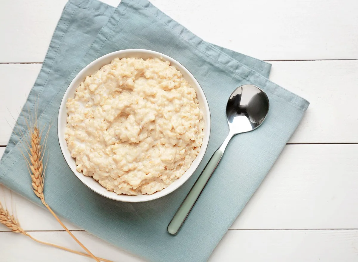 Bowl with tasty oatmeal on white wooden table