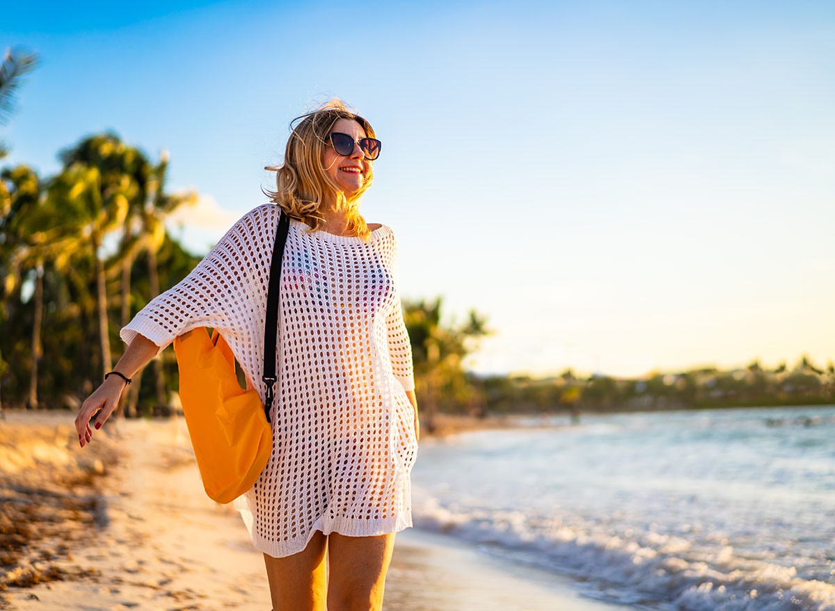 Beach holiday - woman walking on sunny, tropical beach in the morning
