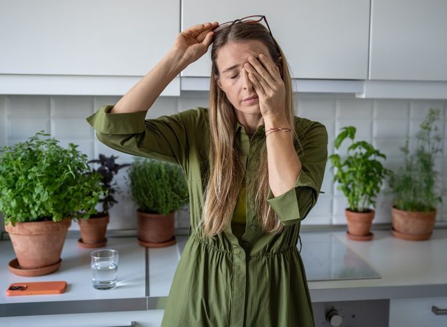 Sleepy woman suffering from chronic fatigue rubbing eyes on kitchen at home. Tired middle aged female feeling bad from lack of rest, headache, lack of energy after party, sleepless night.