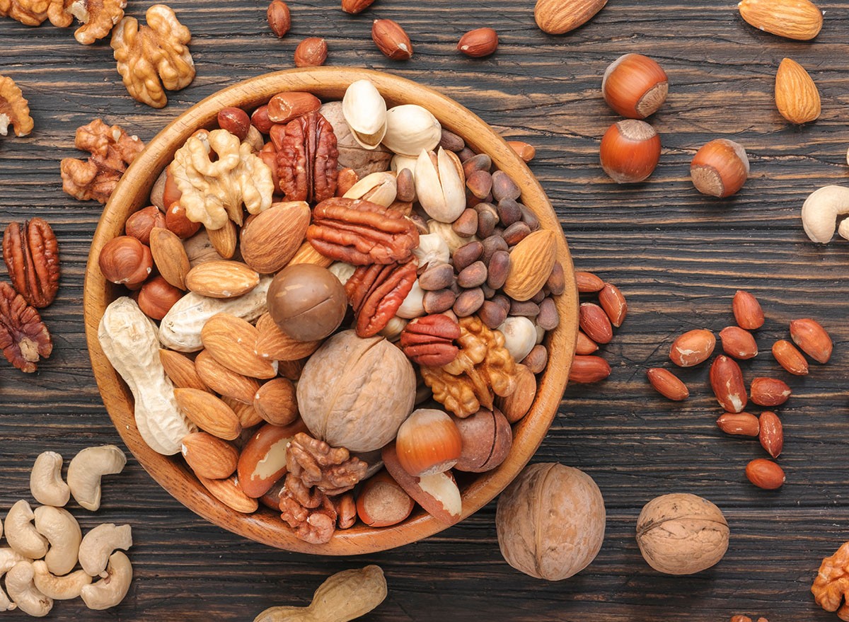 Assortment of nuts in bowls. Cashews, hazelnuts, walnuts, pistachios, pecans, pine nuts, peanuts, macadamia, almonds, brazil nuts. Food mix on wooden background, top view, copy space