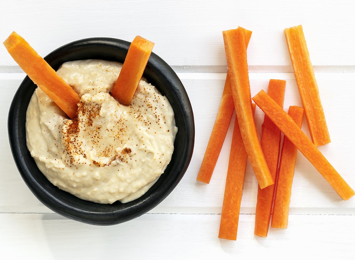 Hummus with carrot sticks. Top view over white timber.
