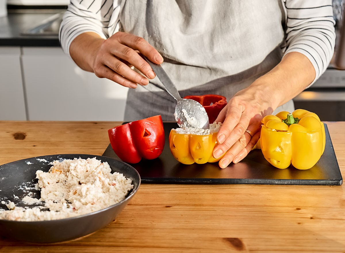 Woman food blogger preparing stuffed colorful bell peppers with ricotta cheese for Halloween party. Peppers carved like Jack-o-lantern scary face. Halloween food idea.
