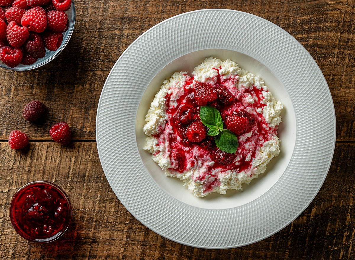 Fresh white cottage cheese with sour cream and red raspberry jam on wooden background, close up, top view