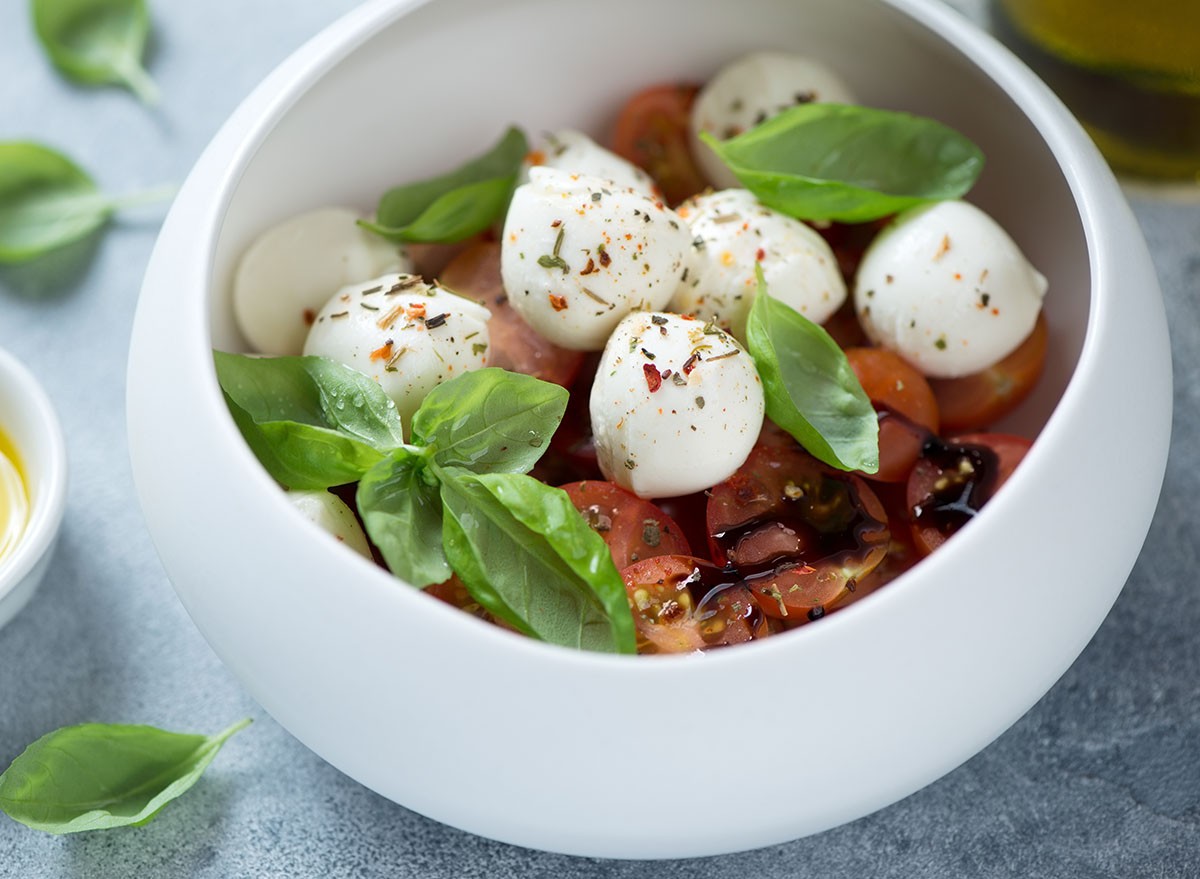 Close-up of caprese salad with mini mozzarella balls, red cherry tomatoes and fresh green basil served in a white bowl, studio shot