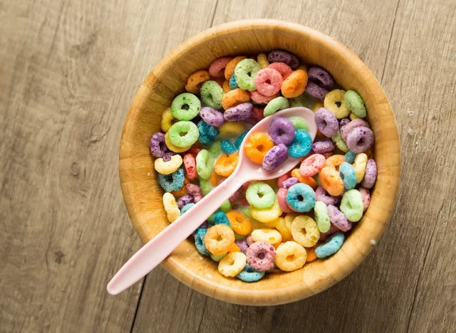 Fruity cereal in a bowl with milk and pink spoon in a wooden background