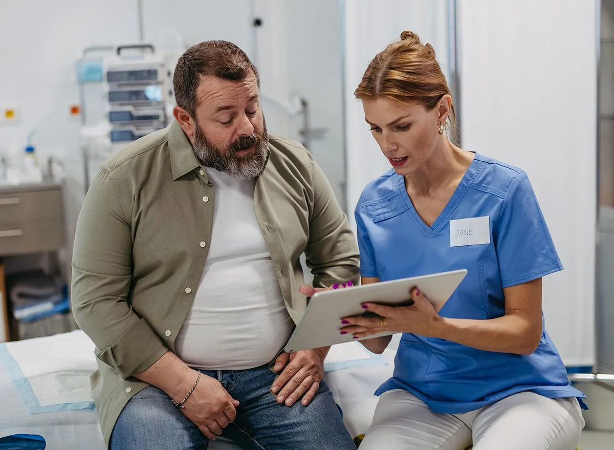 Female doctor consulting with overweight patient, discussing test result in doctor office. Obesity affecting middle-aged men's health. Concept of health risks of overwight and obesity.