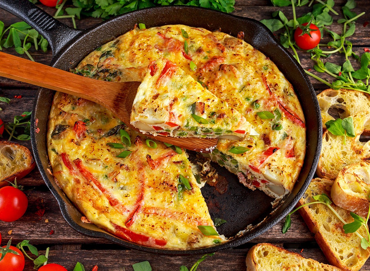 Frittata made of eggs, potato, bacon, paprika, parsley, green peas, onion, cheese in iron pan. on wooden table.