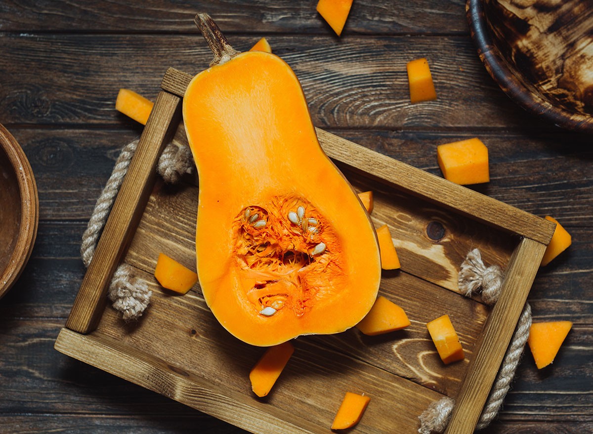 Overhead shot of butternut squash with seeds on rustic wooden tray. Pumpkin pieces, harvest, fall. Dark brown background. Cooking in autumn. Healthy food.