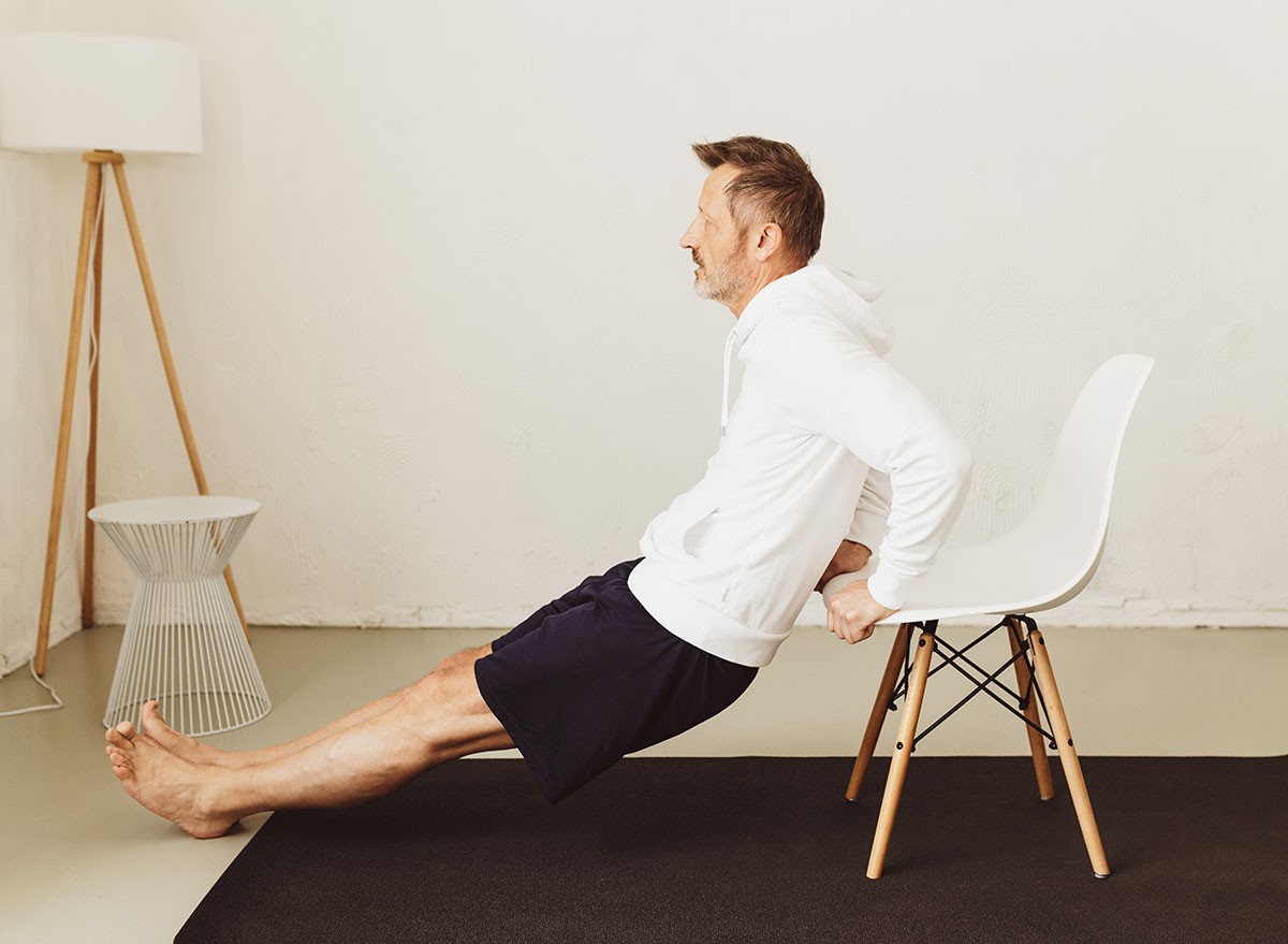 Side view of a determined middle-aged man exercising tricep dips or triceps extension with a chair as workout routine for the arms at home during pandemic