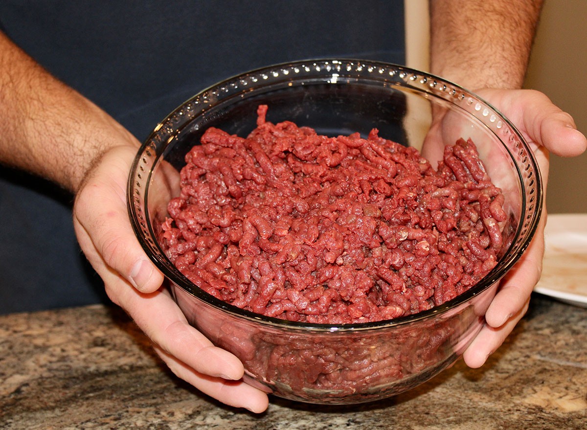 A stainless steel meat grinder that is grinding up fresh venison to make chopped meat. The ground venison is coming out the machine and going into a big glass bowl.