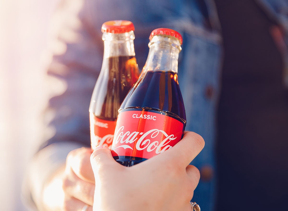 clink drink Coca Cola glass bottle in hands, sunset, soda, junk