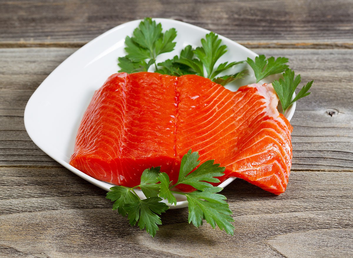 Closeup horizontal photo of fresh red salmon fillet on white plate with parsley on the side and rustic wood underneath