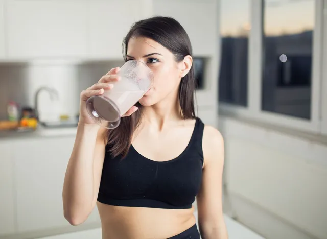 Woman in sportswear drinking sweet banana chocolate protein powder milkshake smoothie.Drinking protein after workout.Whey,banana and low fat milk sport nutrition diet after gym.Healthy lifestyle