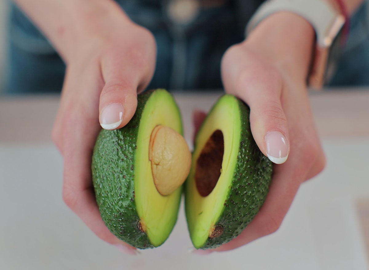 Close-up of a woman holding half of fresh ripe avocado in hand, top view. avocados