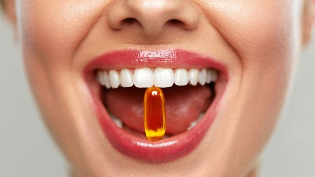 Vitamins And Food Supplements. Close Up Of Beautiful Woman Opened Mouth Holding Fish Oil Pill In White Teeth. Smiling Girl Holding Capsule With Omega-3 Between Teeth. Healthy Diet Nutrition Concept