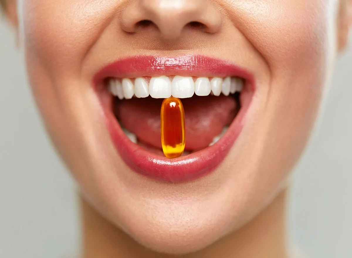 Vitamins And Food Supplements. Close Up Of Beautiful Woman Opened Mouth Holding Fish Oil Pill In White Teeth. Smiling Girl Holding Capsule With Omega-3 Between Teeth. Healthy Diet Nutrition Concept