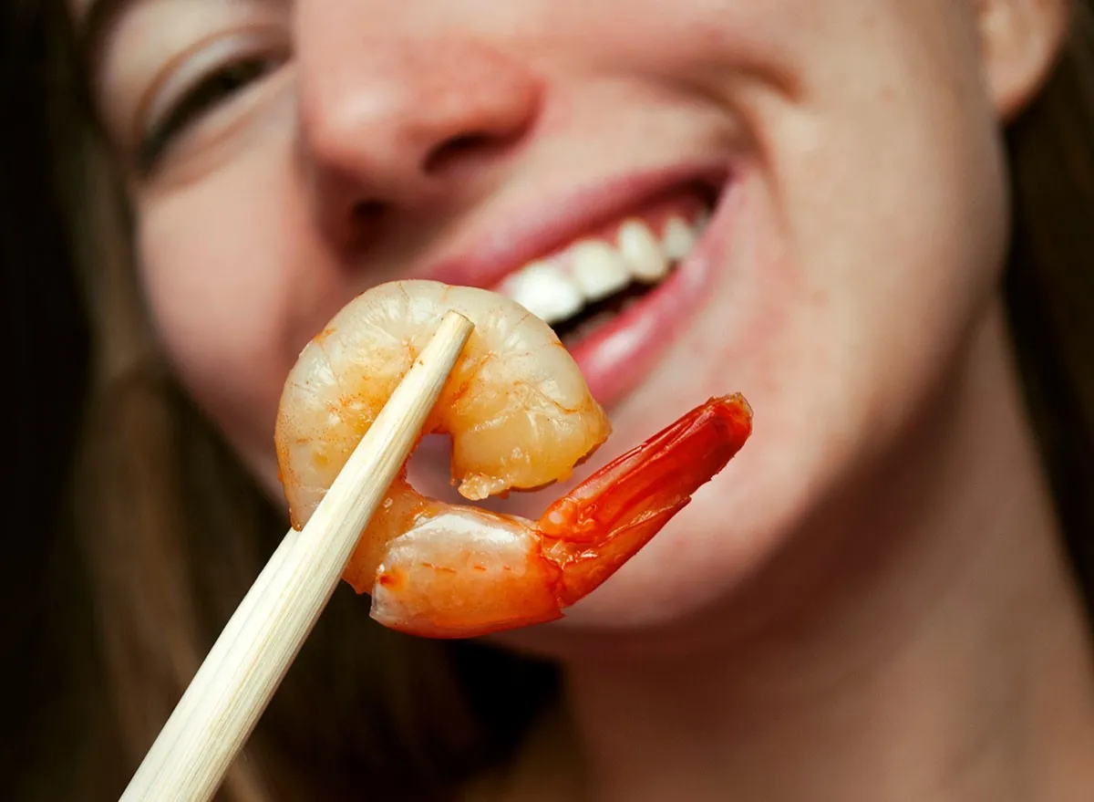 Happy woman smiles and shows fried shrimp to the camera. Eating shrimp with chopsticks. Selective focus. 