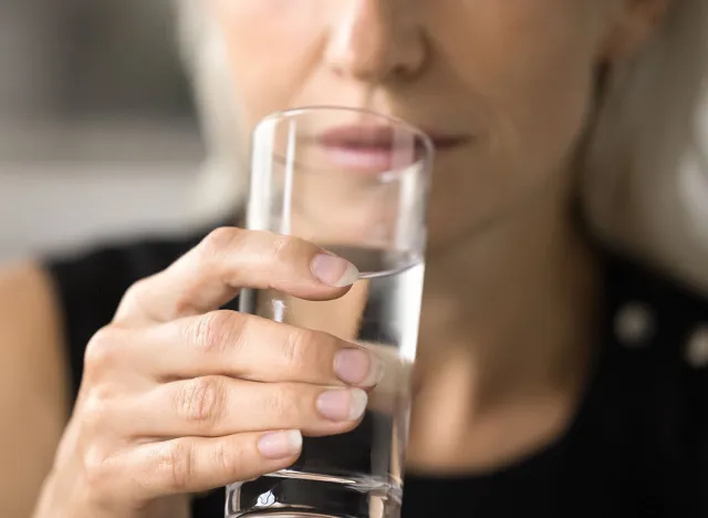 Transparent glass of pure fresh clean mineral water in mature female hand. Cropped shot of woman drinking water, keeping healthy hydration balance, detox diet. Close up focus on object