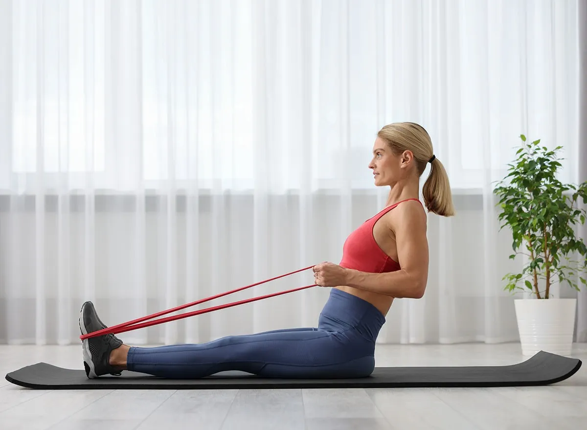Athletic woman doing exercise with fitness elastic band on mat at home