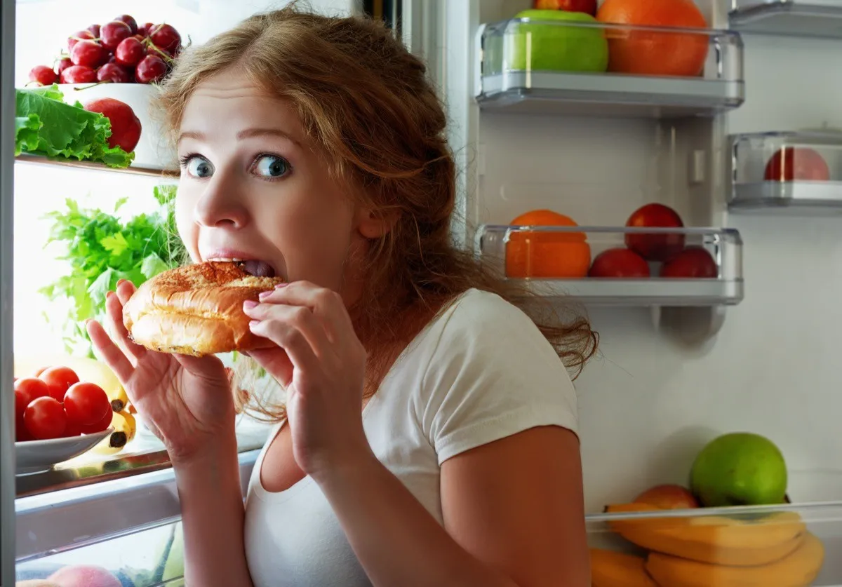 woman eats sweets at night to sneak in a refrigerator. Fridge