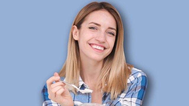 Young attractive woman with tasty yogurt near fridge