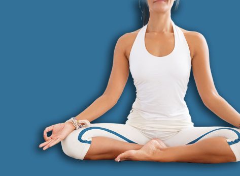Yoga and meditation. An unidentified young woman meditating while practicing yoga at home sitting in lotus pose and folding arms in front