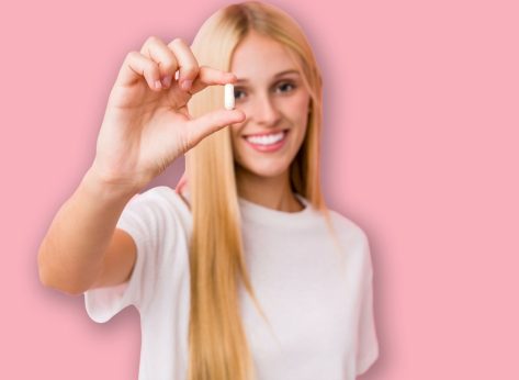 Young blonde woman taking some pills isolated on a blackground