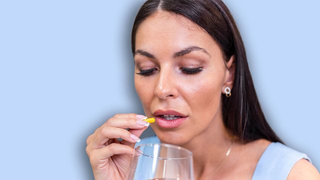 Young woman takes pill with glass of water in hand. Stressed female looking in window and drinking sedated antidepressant meds. Woman feels depressed, taking drugs. Medicines at work