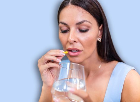 Young woman takes pill with glass of water in hand. Stressed female looking in window and drinking sedated antidepressant meds. Woman feels depressed, taking drugs. Medicines at work