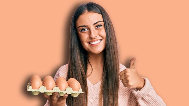 Beautiful hispanic woman holding try of eggs smiling happy and positive, thumb up doing excellent and approval sign