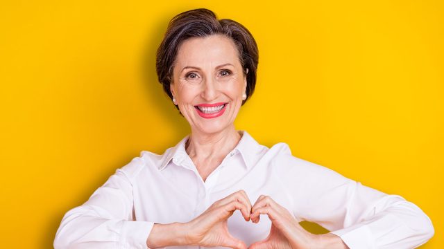 Photo of pretty shiny mature lady wear white clothes smiling showing fingers heart isolated yellow color background