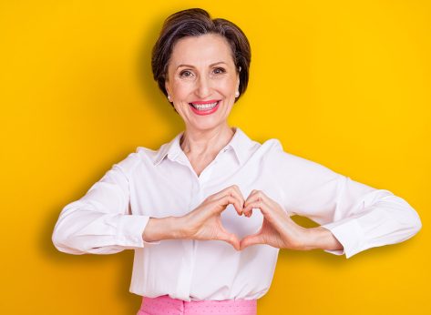 Photo of pretty shiny mature lady wear white clothes smiling showing fingers heart isolated yellow color background