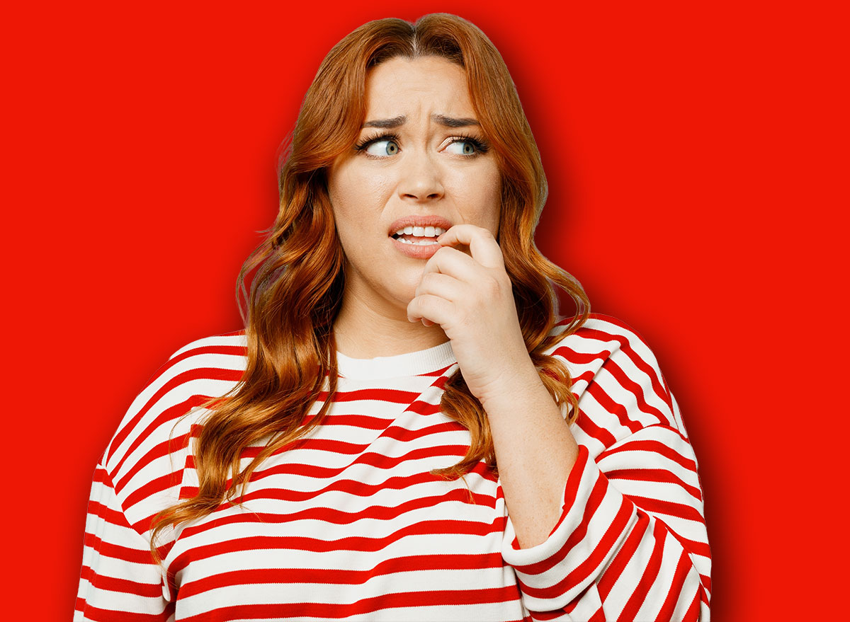 Young sad confused chubby overweight woman she wear striped red shirt casual clothes look aside biting nails fingers isolated on plain pastel light blue background studio portrait. Lifestyle concept