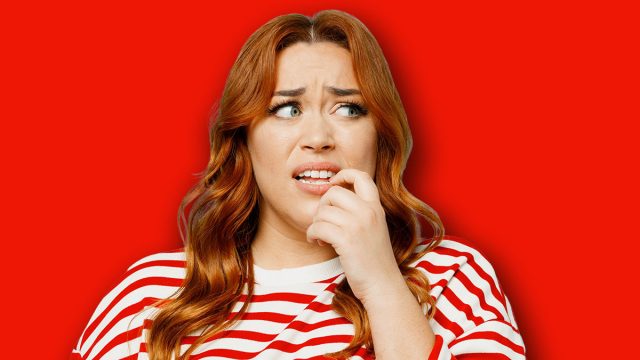 Young sad confused chubby overweight woman she wear striped red shirt casual clothes look aside biting nails fingers isolated on plain pastel light blue background studio portrait. Lifestyle concept