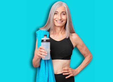 middle age white hair woman smiling happily with a hand on hip and confident with a towel and water bottle. fitness concept
