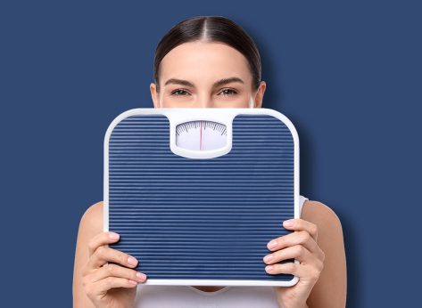 Diet and weight loss concept. Young woman with floor scale on white background
