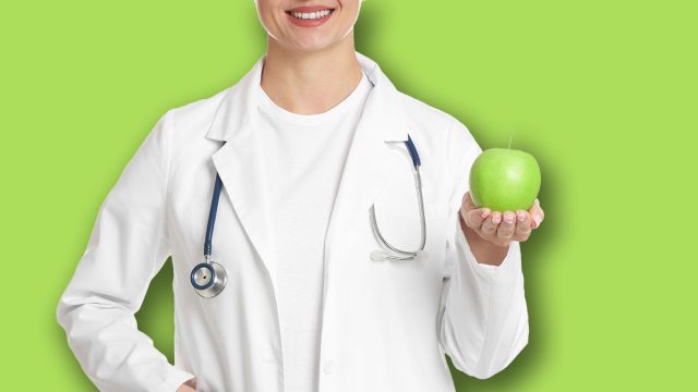 Nutritionist with green apple and stethoscope on white background