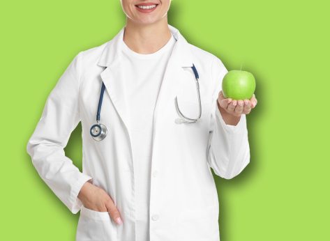 Nutritionist with green apple and stethoscope on white background