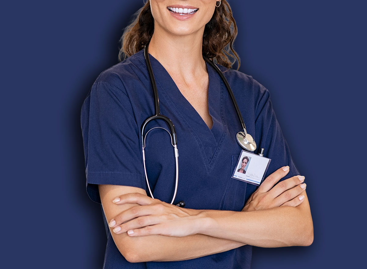 Portrait of happy young female nurse with folded arms standing in hospital hallway. Confident doctor woman in uniform and stethoscope looking at camera with copy space. Young healthcare worker working