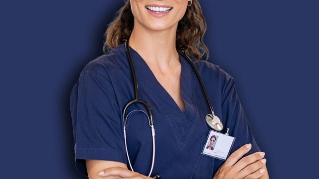 Portrait of happy young female nurse with folded arms standing in hospital hallway. Confident doctor woman in uniform and stethoscope looking at camera with copy space. Young healthcare worker working