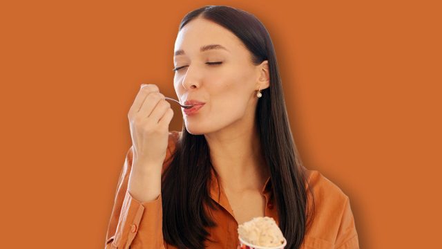 Happy young woman enjoy eating tasty ice cream with closed eyes, sitting in kitchen interior at home, free space